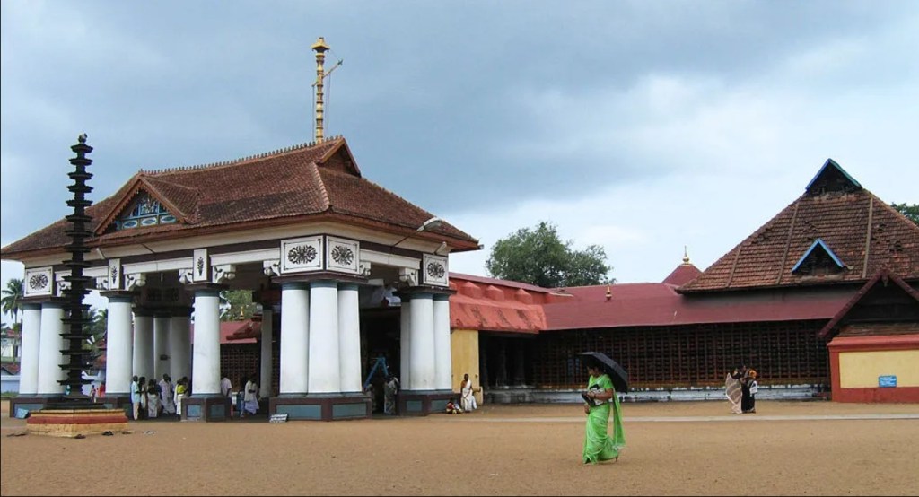 Exterior view of a traditional temple featuring tall columns and ornate roofing, with visitors present in the courtyard, under a cloudy sky.