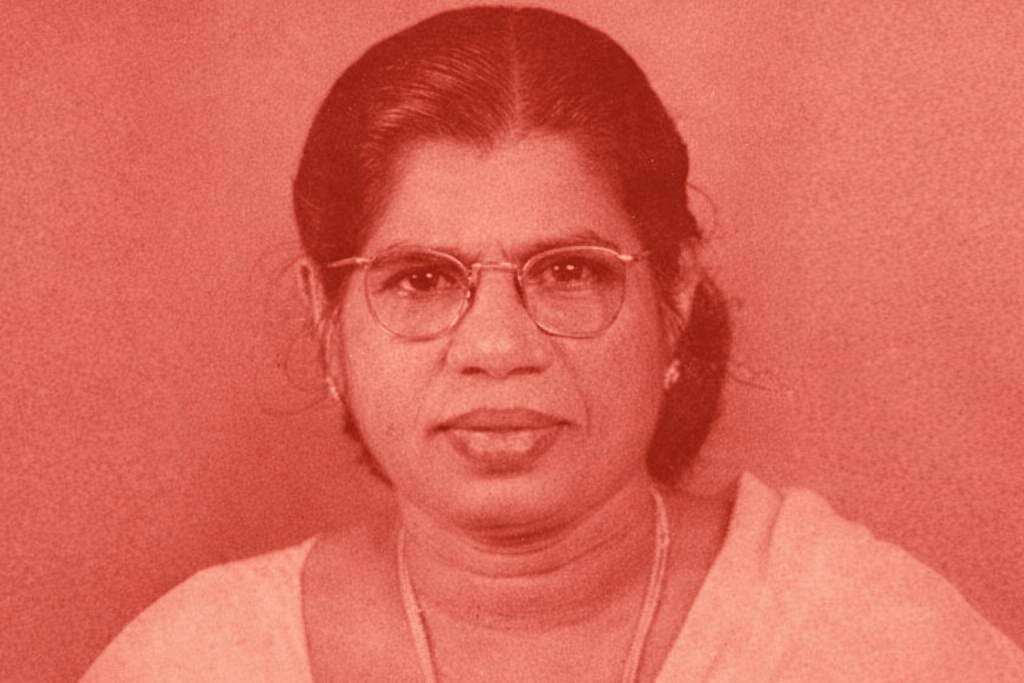 A portrait of a woman with glasses, wearing a light-coloured traditional outfit, set against a red background.