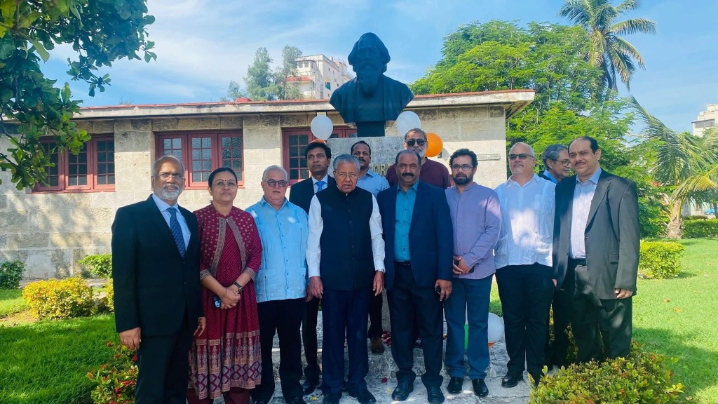 A group of people posing in front of a statue, with greenery and a building in the background.