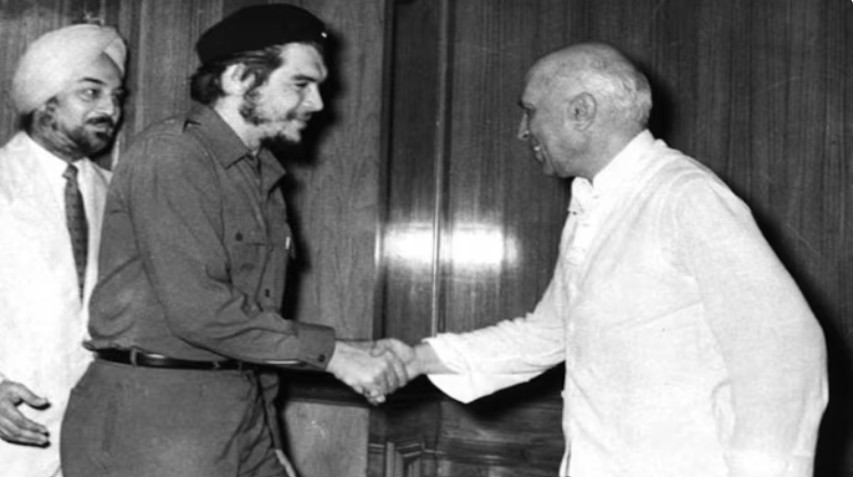 Che Guevara shaking hands with Jawaharlal Nehru, with another man in a turban looking on, in a formal setting.