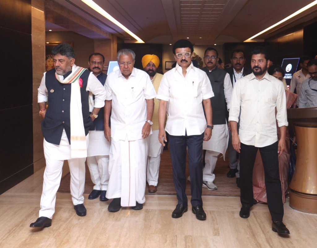A group of men walking together in a hotel lobby, dressed in formal attire. Some are wearing traditional Indian clothing, while others are in western-style suits. They are surrounded by people and a modern interior.